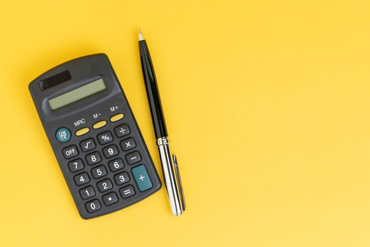Flat lay or top view of black pen with calculator on vivid yellow background table with blank copy space, math, cost, tax or investment calculation