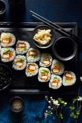 vegan sushi with tofu in General Tso sauce, avocado and fresh vegetables . on a table with branches of a blossoming tree