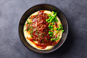 Mashed potatoes with beef meat and green peas in bowl. Dark background. Top view.