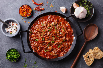 Beef shredded meat with sauce in black pan. Grey background. Top view.