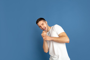 Naklejka premium Singing like celebrities, stars. Caucasian young man's portrait on blue studio background. Beautiful male model in casual style, pastel colors. Concept of human emotions, facial expression, sales, ad.