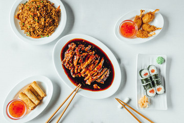 Asian food on white plates, bright background with sweet chicken, sushi, spring rolls.