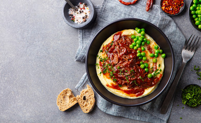 Mashed potatoes with beef meat and green peas in bowl. Grey background. Copy space. Top view.