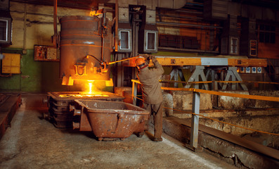 Fototapeta na wymiar Steelmaker pours liquid metal from basket, factory