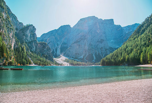 Free space for inscription text poster backdrop of Italian lake of Braies boats float on emerald water Alps in sun light green forest on side mountains tourists relax fantastic nature. Photo wallpaper