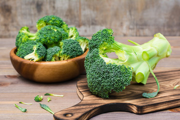 Ready to eat fresh uncooked broccoli on a cutting board and divided into inflorescences in a wooden plate behind on a wooden table. Healthy lifestyle, nutrition and zero waste concept. Close-up