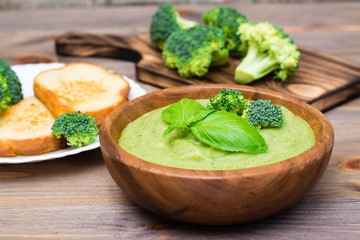 Ready to eat fresh hot broccoli puree soup with pieces of broccoli and basil leaves in a wooden plate on a wooden table. Healthy eating and lifestyle.
