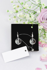 Luxury elegant stylish earrings with natural rock-crystal on a velvet black pillow with flowers roses and petals, mockup, vertical orientation