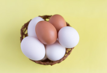 Top view of chicken eggs in an egg basket on yellow. Fresh chicken eggs with copy space. Natural healthy food concept White and one brown egg in a basket.