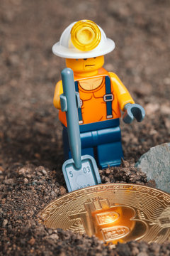 ANKARA, TURKEY. NOVEMBER 17, 2019. Lego mini man miner figurine digging ground with shovel to uncover glowing bitcoin. Cryptocurrency blockchain and mining concept.