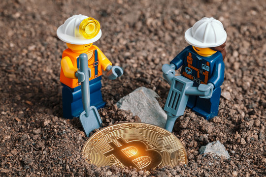 ANKARA, TURKEY. NOVEMBER 17, 2019. Lego mini miner figurines working with tools on ground to uncover glowing bitcoin. Cryptocurrency, blockchain and mining concept.