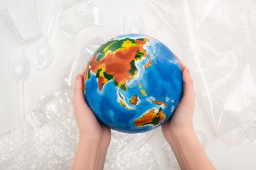 Cropped view of woman holding globe above plastic garbage on white background, global warming...
