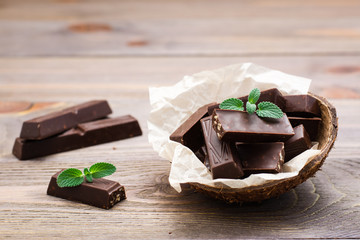 Chocolate pieces and mint leaves in a bowl and on a wooden table. The concept of overweight from...