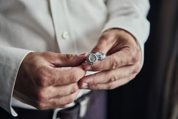 Closeup businessman hands with cufflinks. Man in a business suit, white shirt. Preparing the groom on the wedding day.