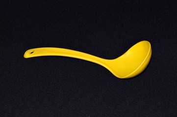 Yellow plastic kitchen spoon or soup ladle isolated on black background