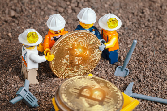 ANKARA, TURKEY. NOVEMBER 17, 2019. Group of Lego mini miner figurines holding shiny bitcoin together and posing. Mining truck loaded with revealed bitcoins. Cryptocurrency, blockchain and mining conce
