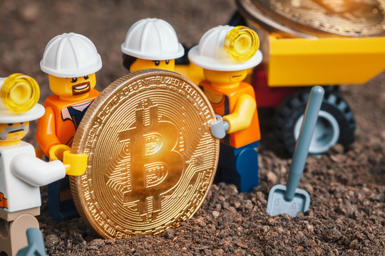 ANKARA, TURKEY. NOVEMBER 17, 2019. Group of Lego mini miner figurines holding shiny bitcoin together and posing. Mining truck loaded with revealed bitcoins. Cryptocurrency, blockchain and mining conce