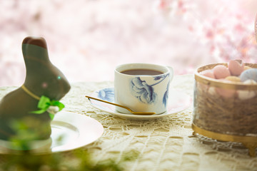 Beautiful served small table with Easter decorations on outdoor terrace. Little chocolate bunny with bow, chocolate eggs, cup of coffee, crystal bowl. Spring holiday setting. Close-up