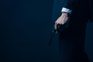 Cropped view of gangster holding gun on dark background