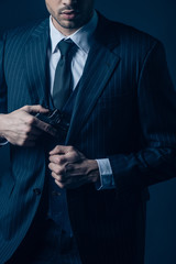 Partial view of gangster hiding weapon in suit on dark blue background