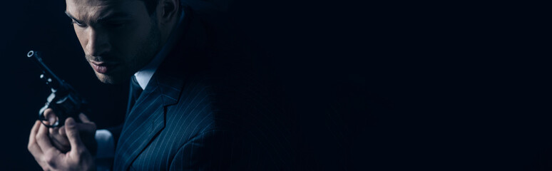 Gangster holding revolver on dark background, panoramic shot