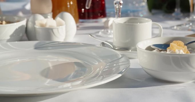 Close up shot of hands of a waiter preparing dishes for client's breakfast at hotel, putting a plate, napkin, fork and knife on table with snacks 4k footage