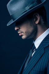 Profile of mafioso in suit and felt hat on dark background