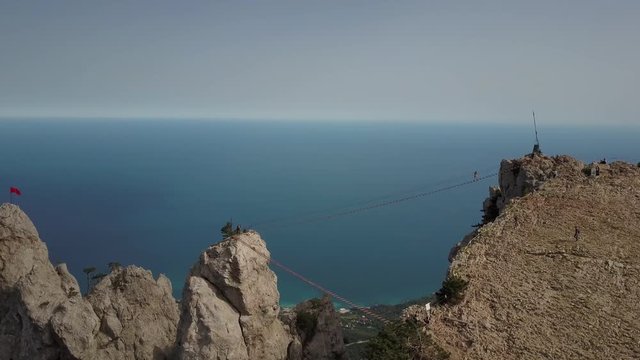 Coming shot of the amazing landscape of the highest mountain Ai-Petri and the Black Sea, Crimea, Ukraine. Top view of tourists walking on extreme bridge upstairs. Stepping over the abyss, top view.