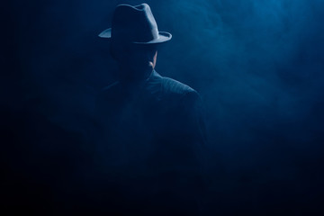 Silhouette of mafioso in felt hat and suit on dark background - obrazy, fototapety, plakaty