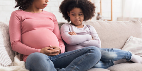 Upset little girl looking at pregnant mother belly with jealousy