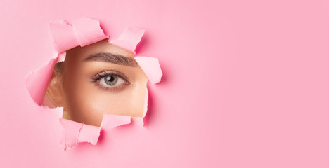 Woman Looking At Camera Through Hole Torn In Pink Paper