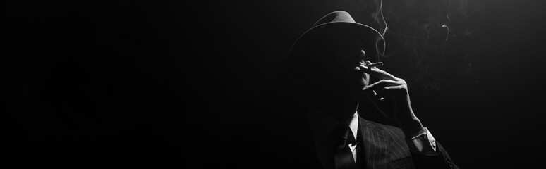 Fototapeta Monochrome image of mafioso silhouette smoking on black background, panoramic shot obraz