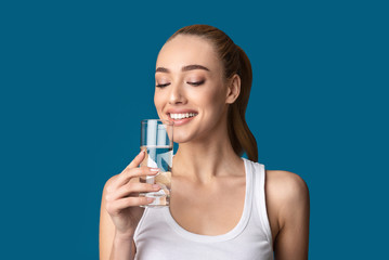 Happy Girl Drinking Glass Of Water Standing On Blue Background