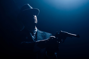 Silhouette of mafioso with outstretched hands aiming gun on dark background