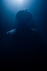 Silhouette of dangerous mafioso in suit and felt hat on dark background