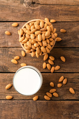 Overhead shot of glass of almond milk on rustic wooden background with almonds in bowl