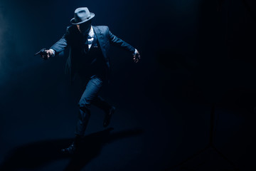 Gangster with outstretched hand aiming revolver and running on dark background