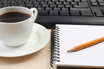 Ceramic cup with coffee and a computer keyboard on a wooden table