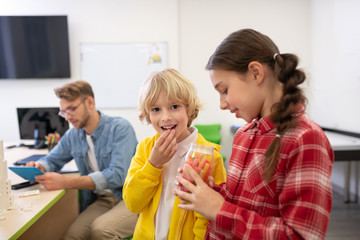 Kids eating sweets, male teacher holding tablet