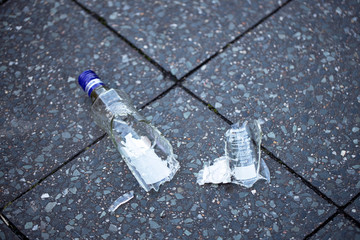 A broken alcohol bottle lies on a concrete tile in the street