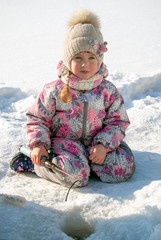 A girl in overalls on a frozen snowy river is fishing. Winter fishing in the ice hole.