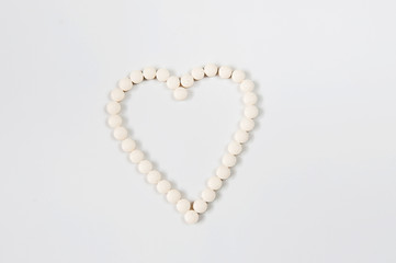 Medicine pills concept on gray background. Round pills in the shape of a heart on a white background close-up and copy space.