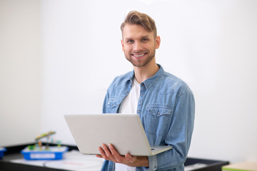 Male teacher standing, holding laptop and smiling