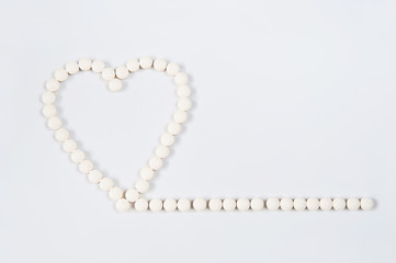 Medicine pills concept on gray background. Round pills in the shape of a heart on a white background close-up and copy space.