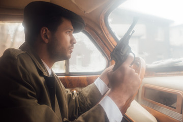 Profile of mafioso in flat cap and coat with gun driving car