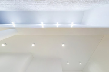 looking up on suspended ceiling with halogen spots lamps and drywall construction in empty room in...