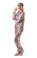Portrait of woman in pajamas, with sleep mask and cup of coffee on white background