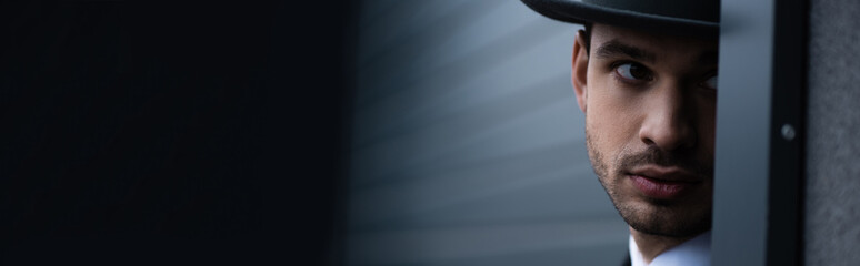 Selective focus of mafioso looking from corner on street, panoramic shot