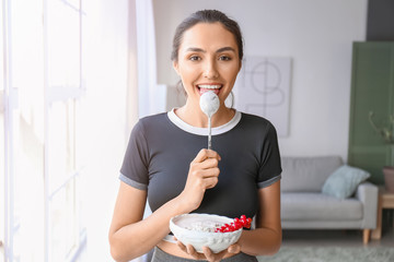 Young woman eating tasty yogurt at home