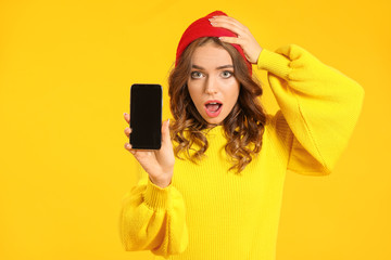 Surprised young woman with mobile phone on color background